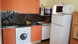 Een kleine keuken met oranje kastjes, een wasmachine, een magnetron en een koelkast.