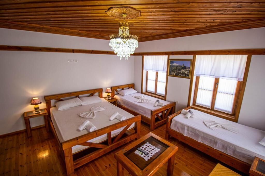 A wooden-floored room with three beds, a chandelier, and windows with curtains.
