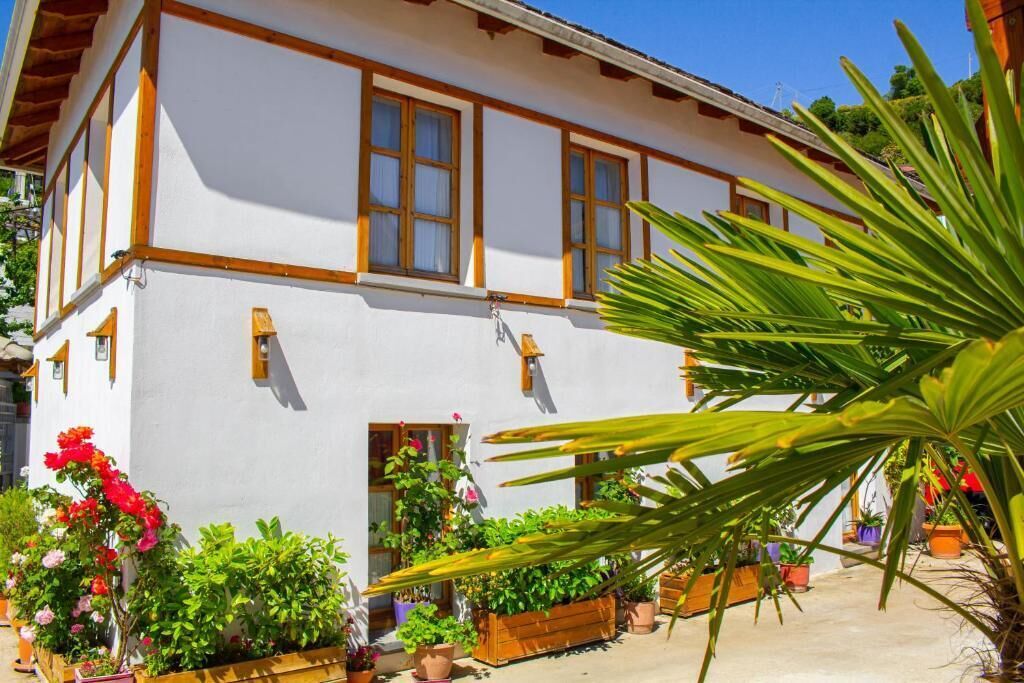 Un edificio blanco con detalles de madera y varias ventanas. Hay plantas y flores en macetas al frente.