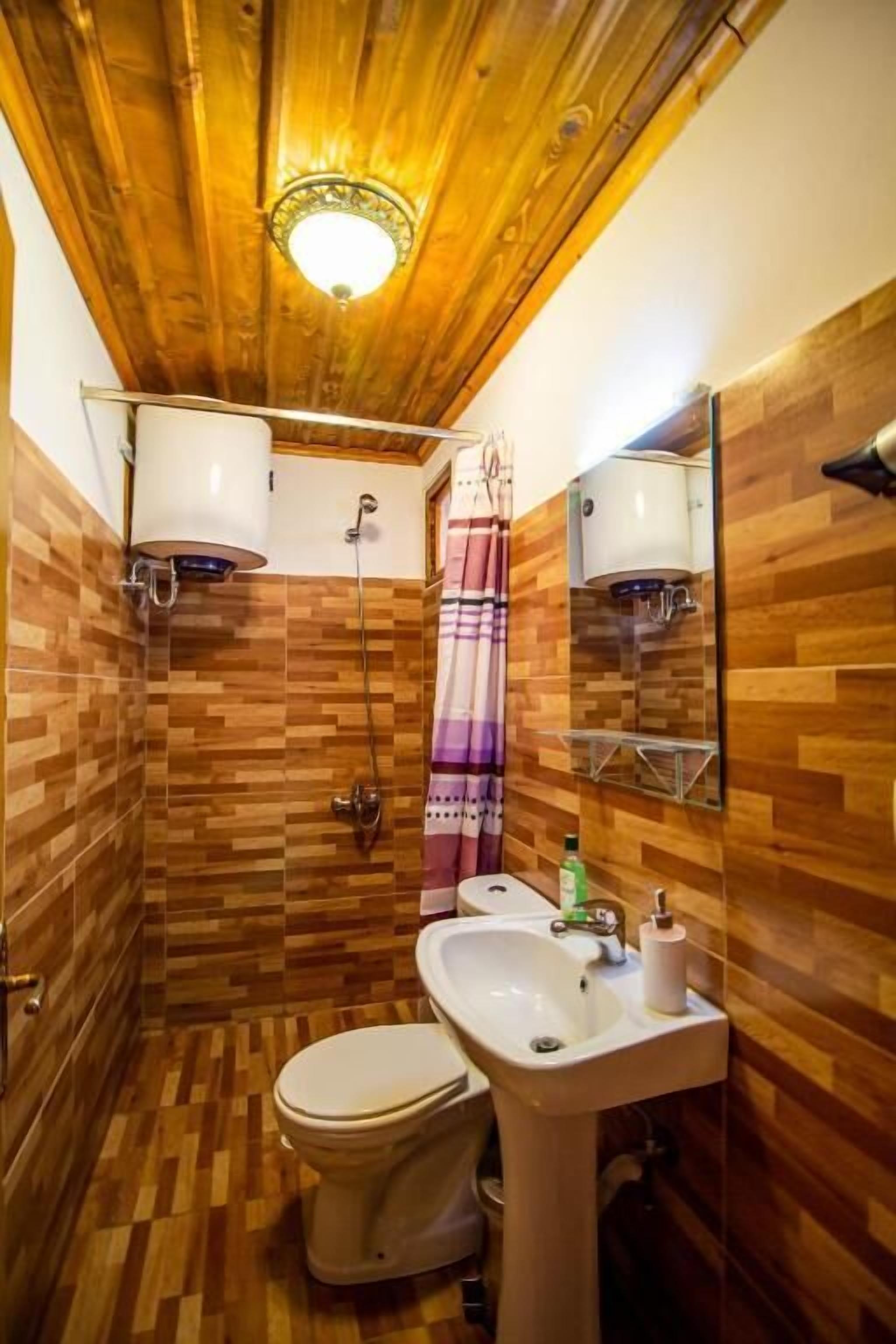 Ein Badezimmer mit Holzvertäfelung, Toilette, Waschbecken, Dusche und Spiegel mit Handtuchhalter.