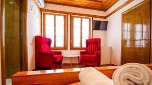 Una habitación con dos sillas rojas, una mesita, un banco de madera y una toalla enrollada sobre el banco.