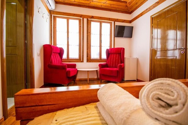 Una habitación con dos sillas rojas, una mesita, un banco de madera y una toalla enrollada sobre el banco.