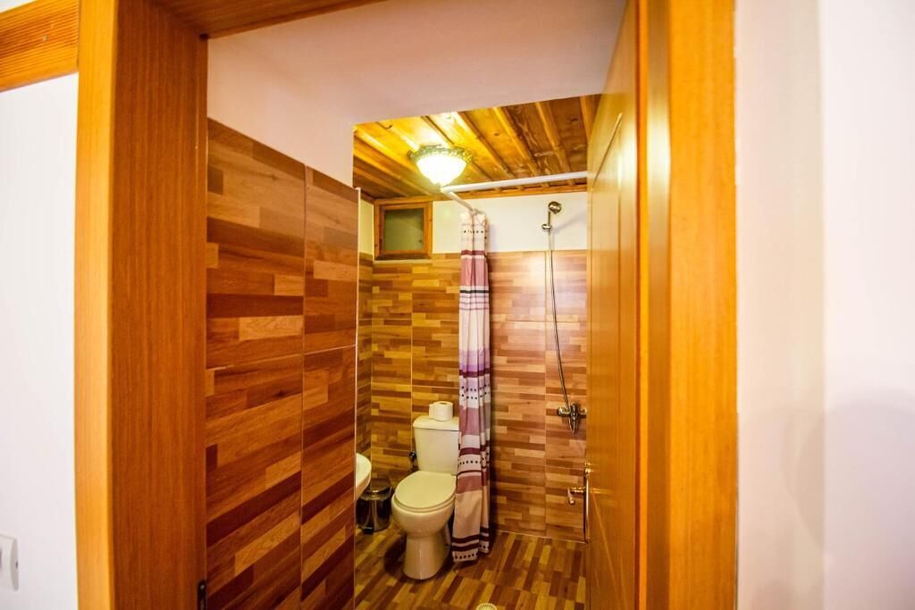 A compact bathroom with a wooden floor, a toilet, a shower, and a towel hanging on the wall.