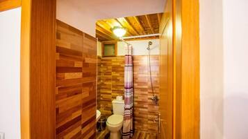A compact bathroom with a wooden floor, a toilet, a shower, and a towel hanging on the wall.