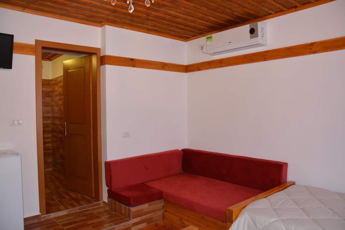 A room with a wooden ceiling, a red sofa, a white bed, and a wooden door.