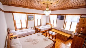Una habitación con dos camas, un banco de madera, una mesita y una araña.