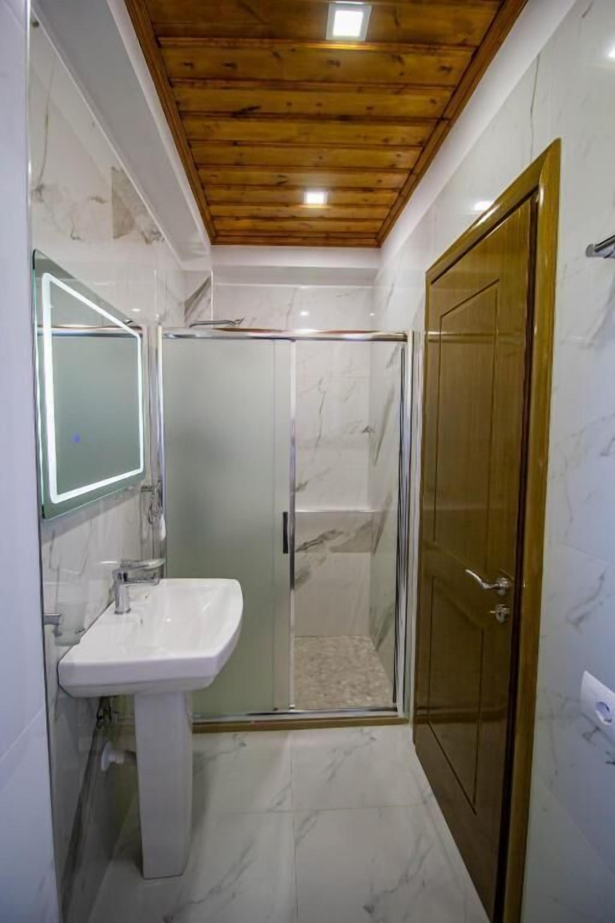 A bathroom with a glass-enclosed shower, a white sink, and a wooden ceiling.