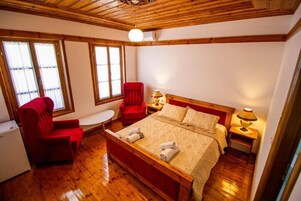 Un dormitorio con una cama de madera, una silla roja, una mesita y una ventana con persianas.