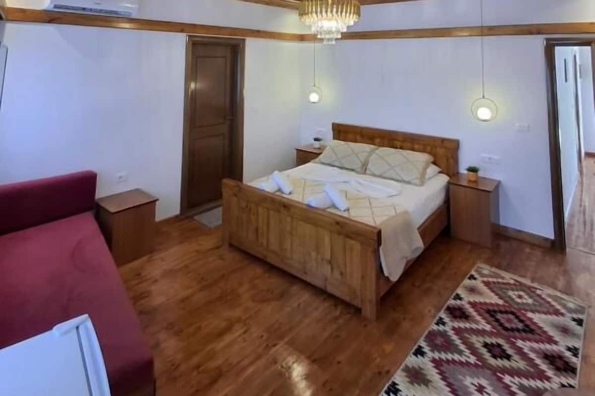 A wooden-paneled bedroom with a bed, bedside tables, a red sofa, and a patterned rug.