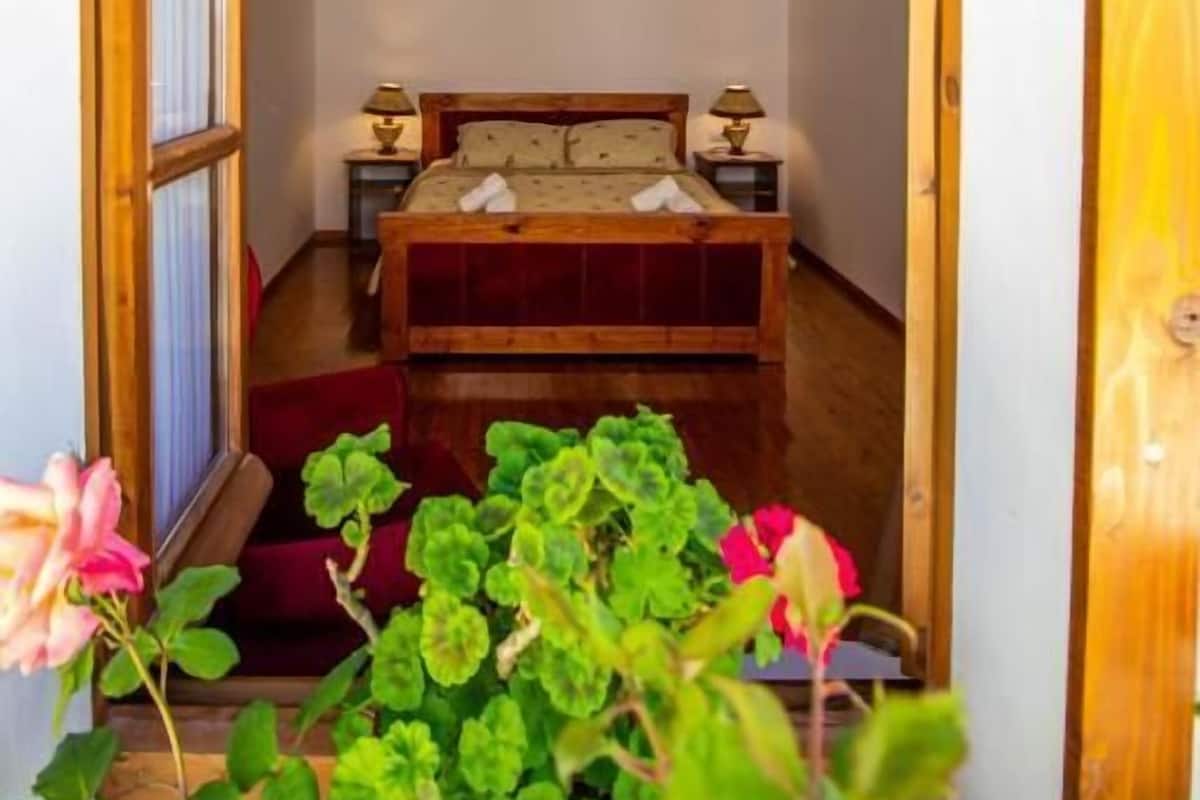 A bedroom with a wooden ceiling, a bed, bedside lamps, and a window.