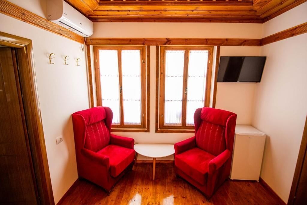 Een kamer met twee rode fauteuils, een kleine witte tafel en een witte koelkast.
