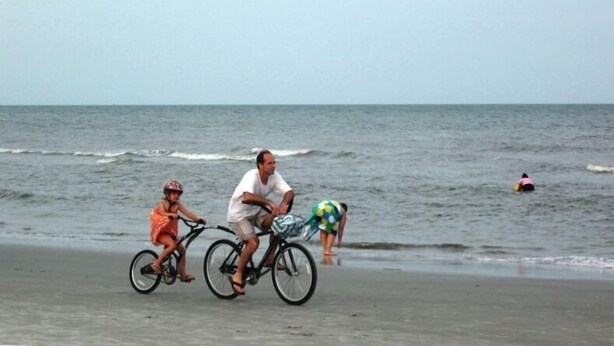 A beach scene with a bicycle, a person in a pink swimsuit, and another in an orange dress. - Spacious Villa Lovely golf course view Free Tennis-PB! 20% Aug 29! (Hilton Head Island)