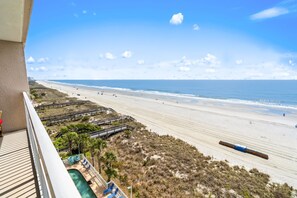 Vista de una playa desde un balcón con piscina, pasarelas de madera y una costa distante.