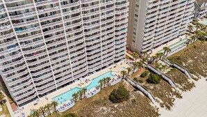 Ein Hochhotel mit mehreren Balkonen, einem Swimmingpool und einem Strandbereich.