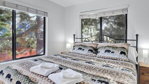 A bedroom with a large bed, two bedside tables, and a window with blinds.