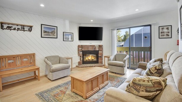 A modern living room with a fireplace, comfortable seating, and a large window offering a view of the outdoors.