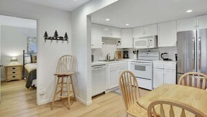 A modern kitchen with white cabinets, stainless steel appliances, and wooden chairs.