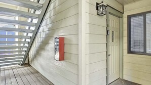 A covered porch with a wooden floor, a white door with a red mailbox, and a lantern on the wall.