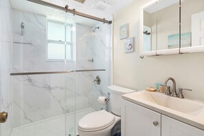 Un bagno con doccia vetrata, un water, un lavabo con specchio sopra e una parete in marmo.