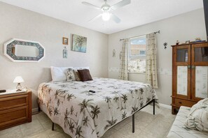 A bedroom with a bed, nightstand, lamp, and a cabinet. - Coastal Cottage with community pool, free parking and boardwalk to beach- SCV 12 (St Augustine Beach)