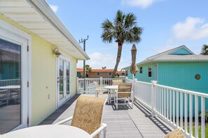 A balcony with outdoor furniture, a palm tree, and a turquoise building in the background. - Coastal Cottage with community pool, free parking and boardwalk to beach- SCV 12 (St Augustine Beach)