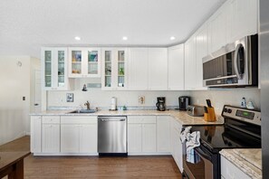 A modern kitchen with white cabinetry, stainless steel appliances, and a granite countertop. - Coastal Cottage with community pool, free parking and boardwalk to beach- SCV 12 (St Augustine Beach)