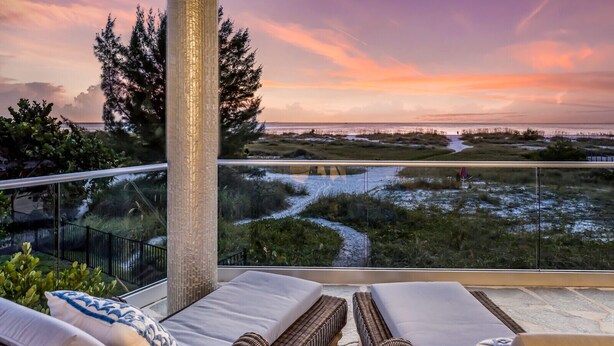 A balcony with lounge chairs, a view of a coastal landscape, and a tall column.