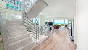 A spacious living area with a staircase, a dining area, and large windows offering a view of the ocean.