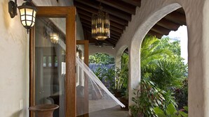 A covered outdoor area with a wooden door, a large vase, and potted plants.