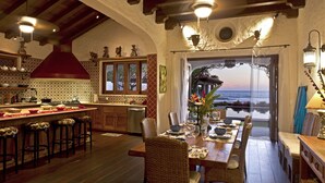A kitchen with a bar area, dining table, and chairs, with a view of the sea through a glass door.