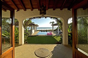 A covered patio with a view of the ocean, a pool, and a flamingo float.