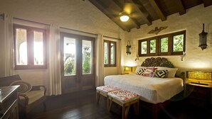 A bedroom with a bed, bench, wooden furniture, and large windows.