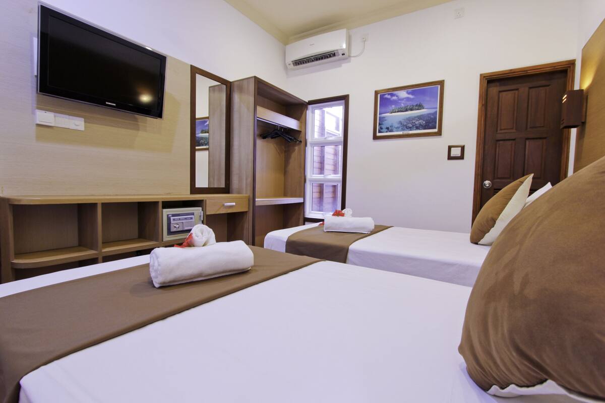 A hotel room with two beds, a TV, a window, and a door.