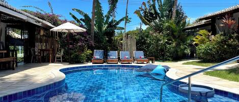 A swimming pool with lounge chairs and umbrellas, surrounded by tropical plants and palm trees.