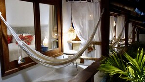 A hammock in a room with a bed, a chair, and a table with a lamp.