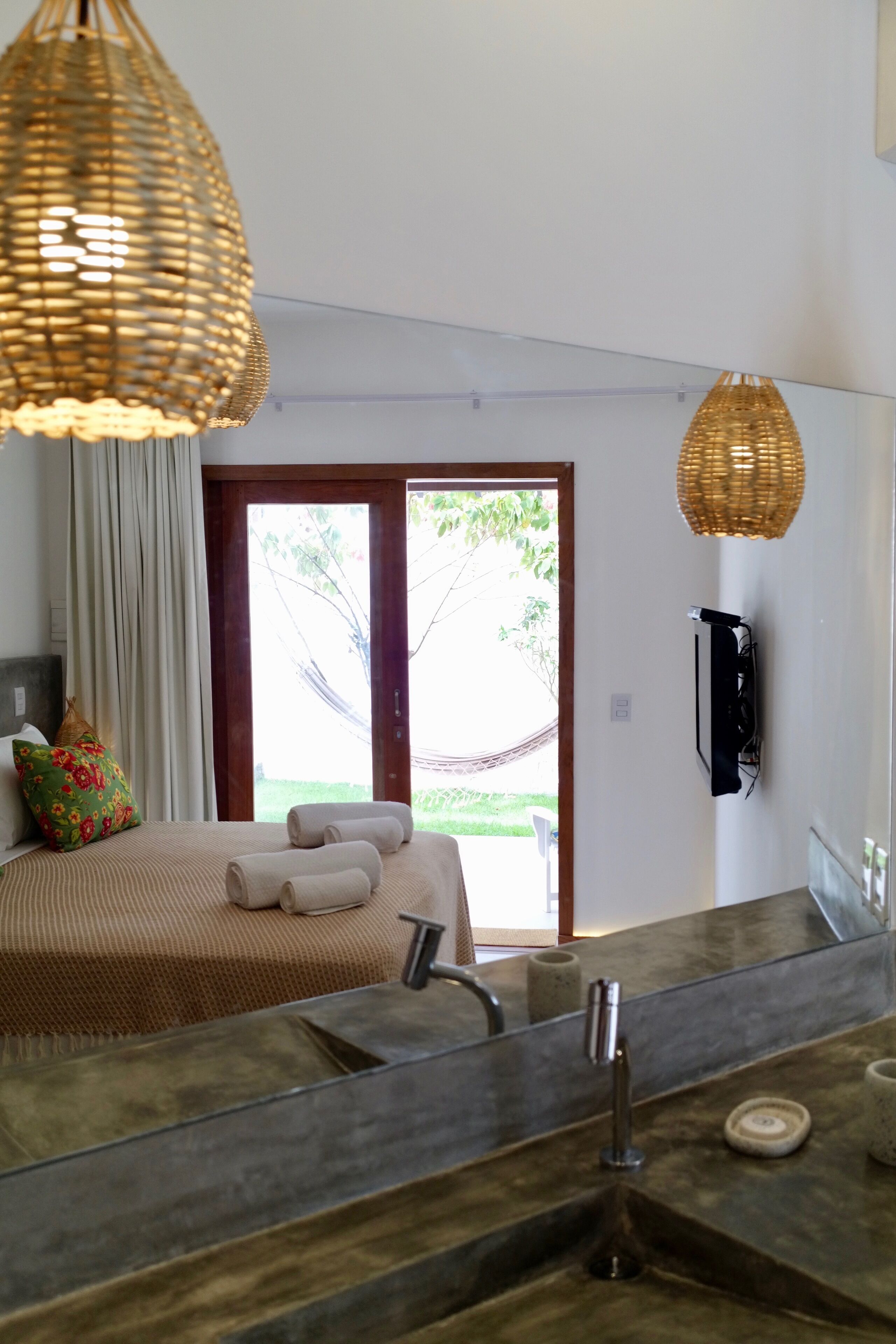 A modern bathroom with a large mirror, a sink, and a shower area. There is a window with a view of greenery outside.