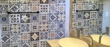 A bathroom with a tiled wall featuring a variety of patterns and a large mirror above a sink.