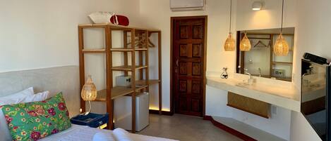 A neatly arranged bedroom with a bed, a wooden shelf, a wardrobe, a mirror, and a hanging light fixture.