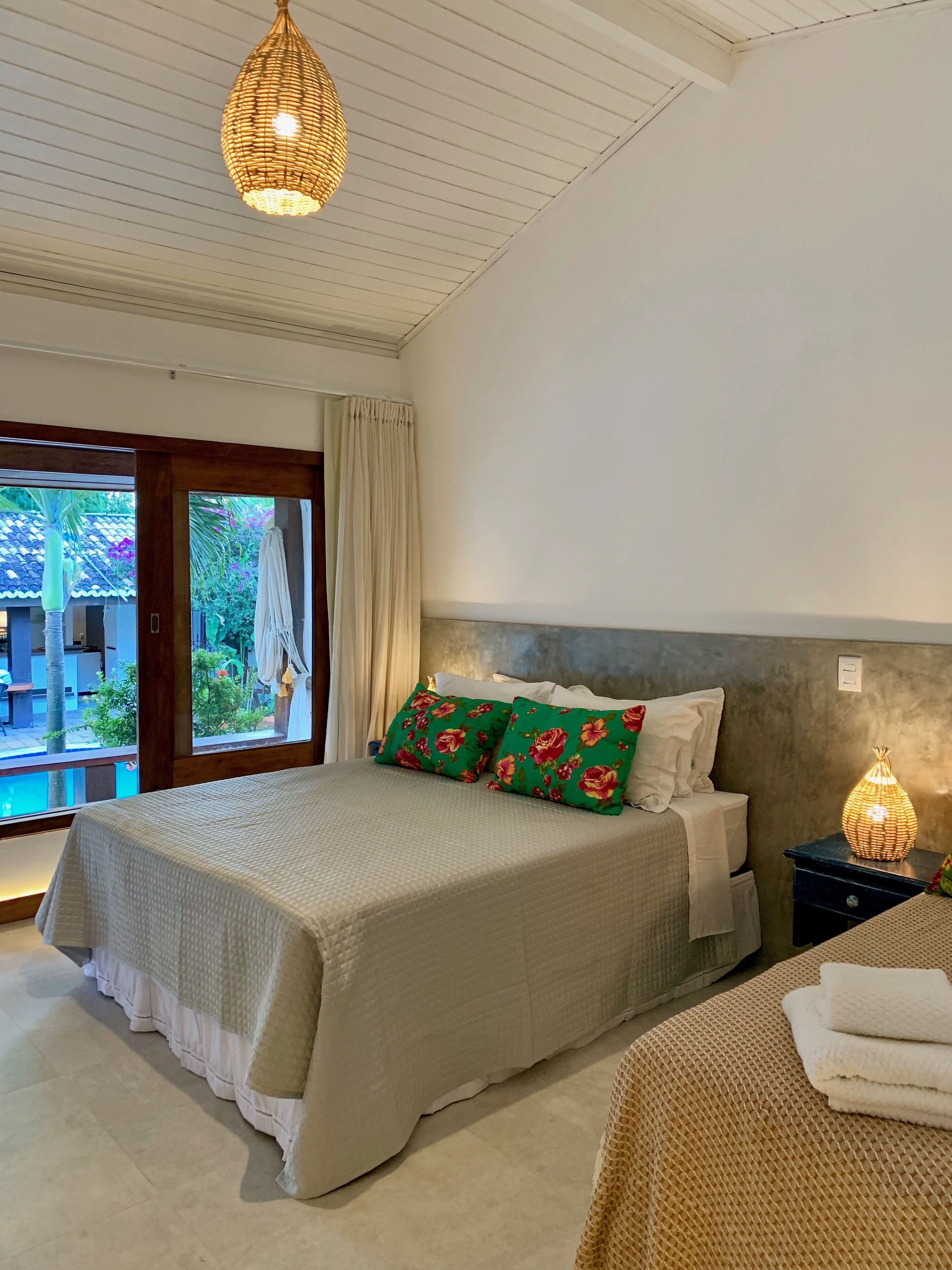 Un dormitorio con una cama grande, una mesita de noche, una lámpara colgante y vistas al exterior.