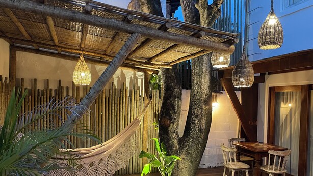 A wooden deck with a hammock, hanging lights, and a table with chairs.