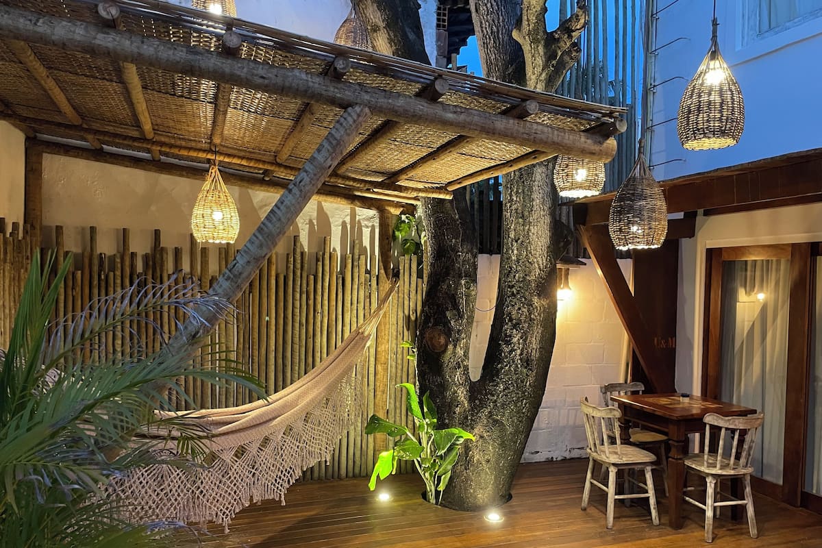 A wooden deck with a hammock, hanging lights, and a table with chairs.