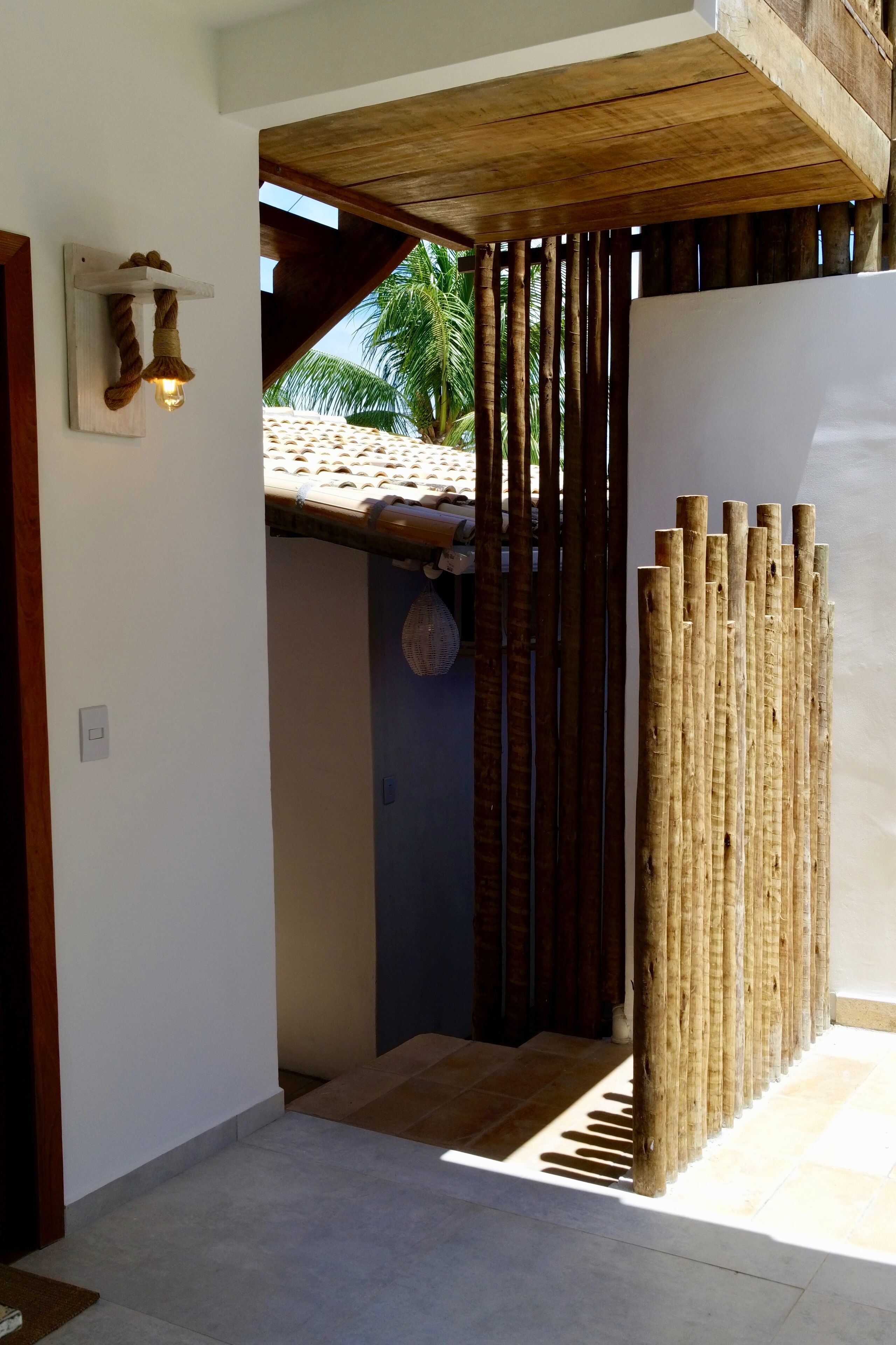 A wooden door with a rope handle, a light fixture on the wall, and a bamboo fence.