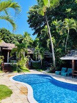 Un área de piscina con bordeado de azulejos, rodeada de palmeras y una hamaca.