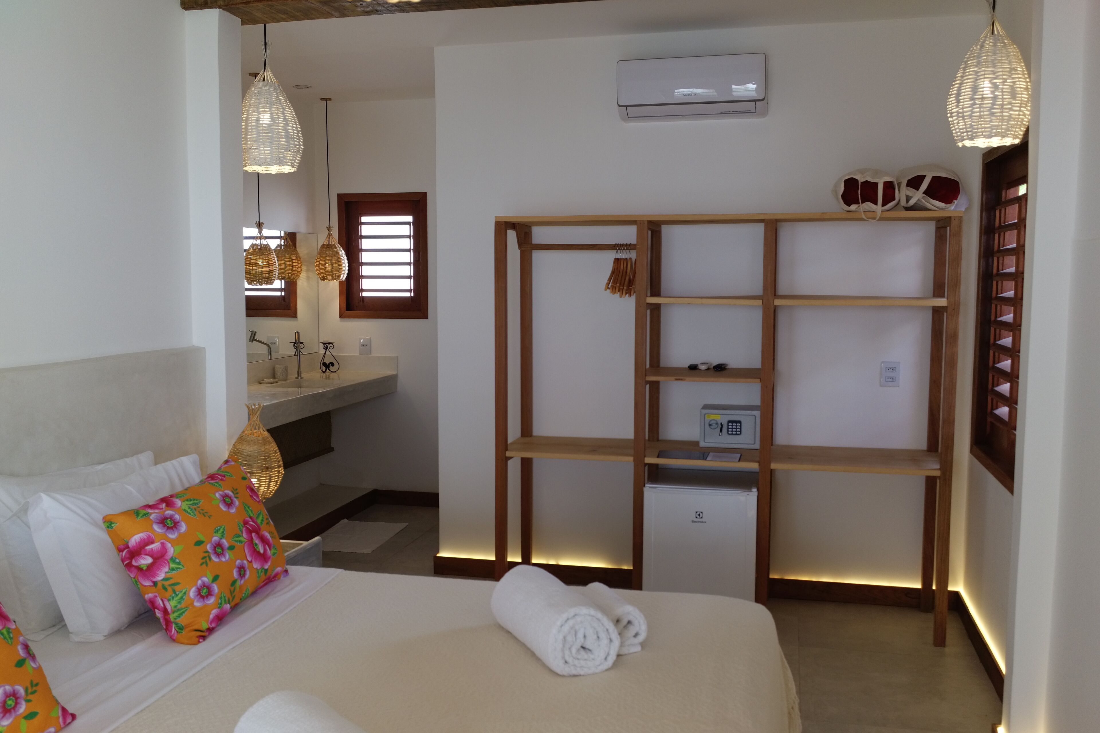 A hotel room with a bed, a wooden shelf unit, a mirror, and a bathroom with a sink and towel rack.