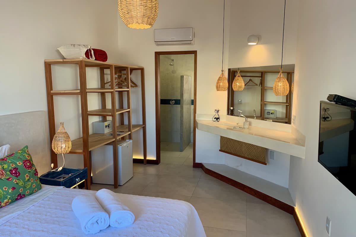 A hotel room with a bed, a wooden shelf, a mirror, a sink, and a shower area.