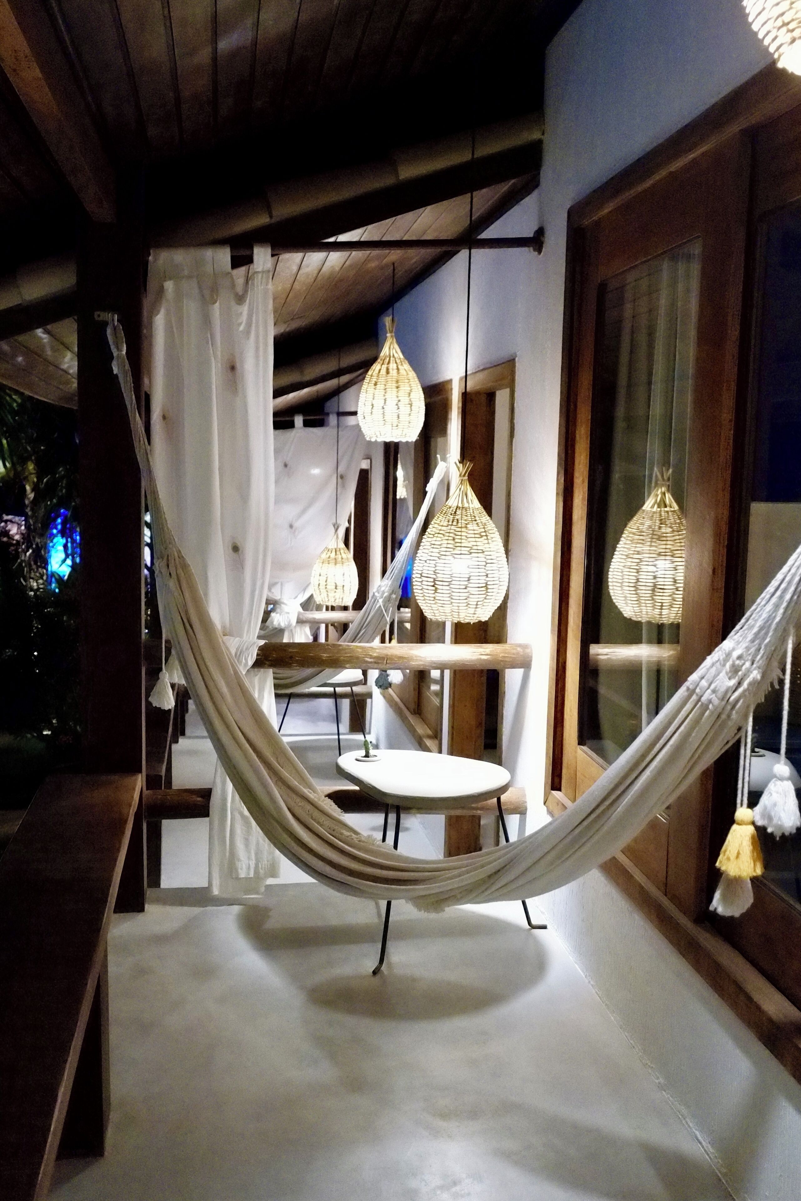 A hammock on a balcony with hanging wicker lamps and a view of the interior.