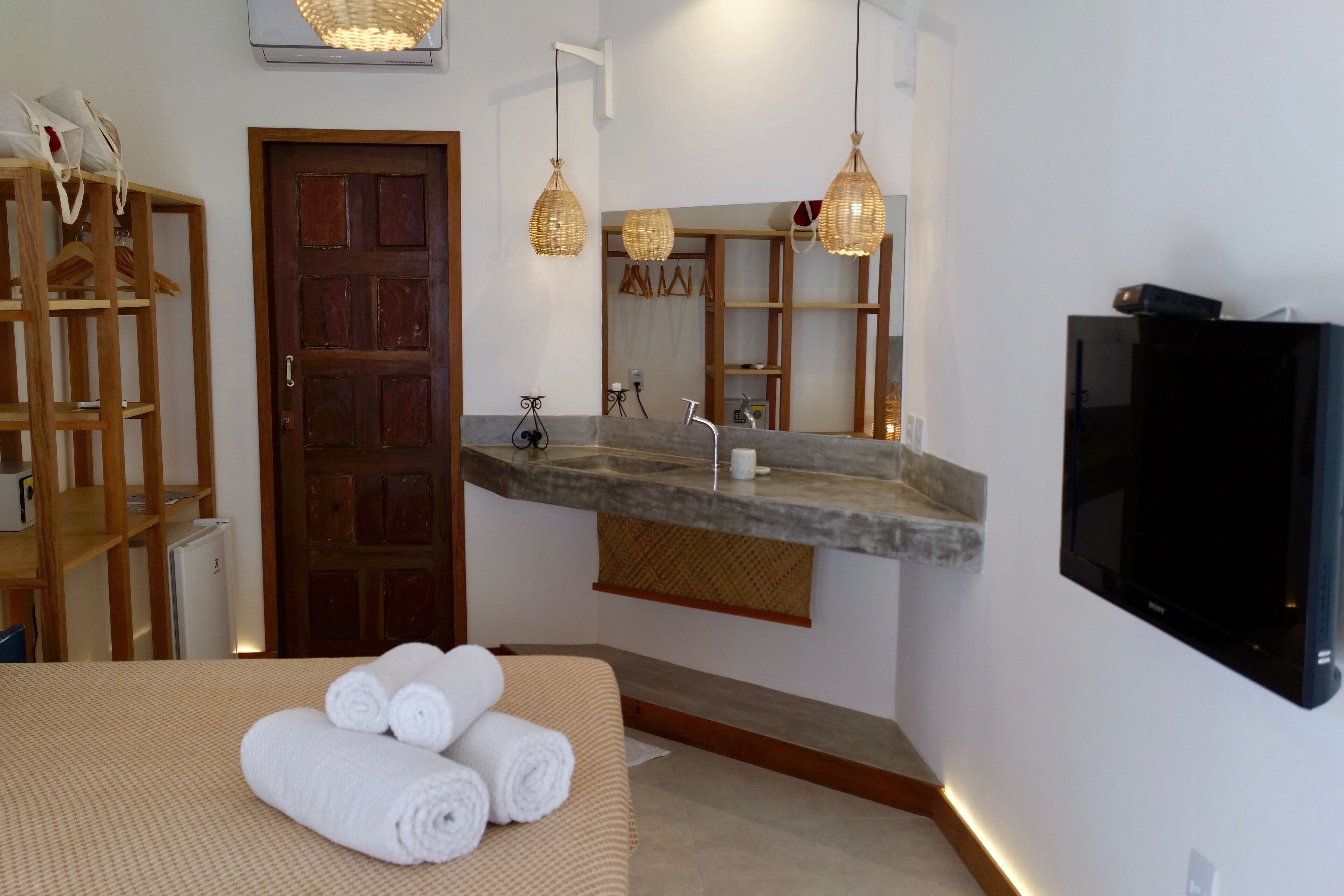 A modern bathroom with a wooden door, a vanity with a mirror, a television, and a bed with rolled towels.