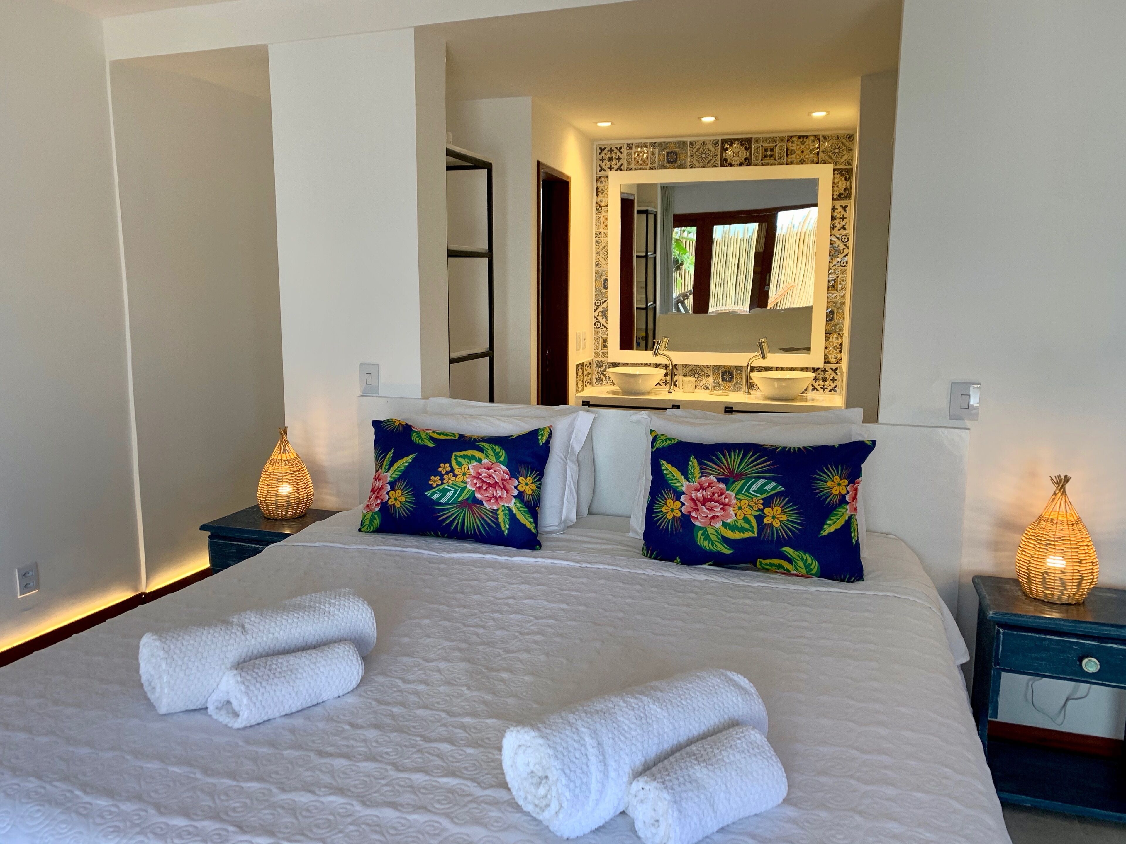 A hotel room with a large bed, two pillows with floral designs, a double sink, and a mirror above the sink.