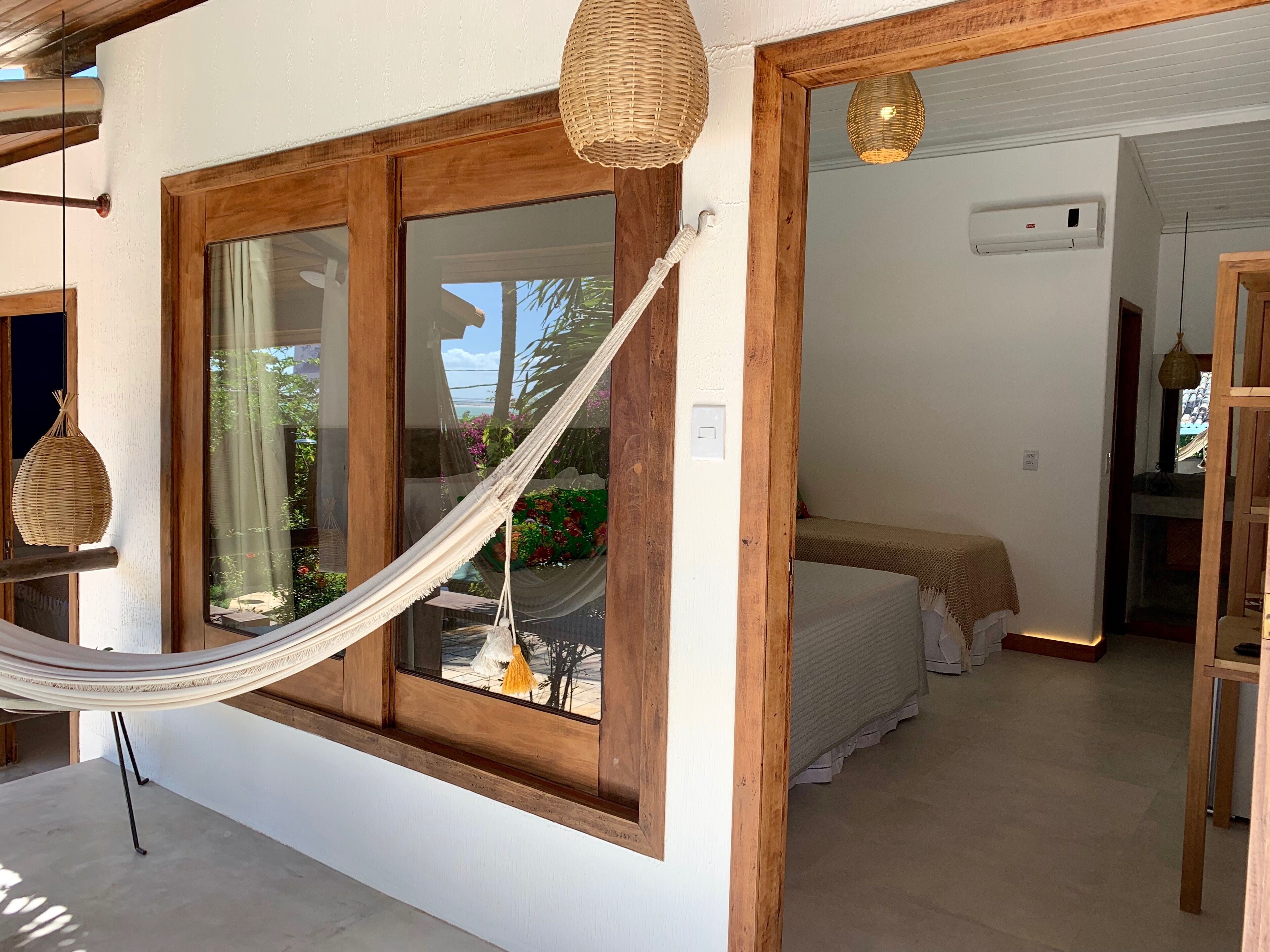 A room with a large window, a hammock, a bed, and a ceiling fan.