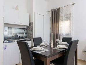 A dining area with a dark wooden table set for four, white plates, and wine glasses. - Apartments Adria (Kastela)